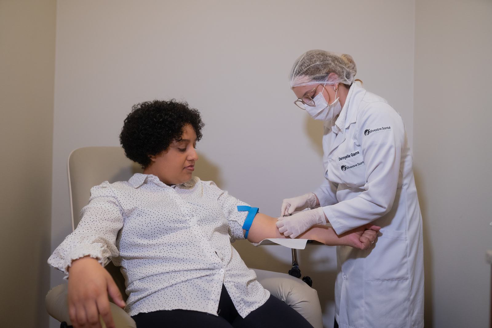 Participante de pesquisa durante coleta de sangue realizada por profissional de jaleco